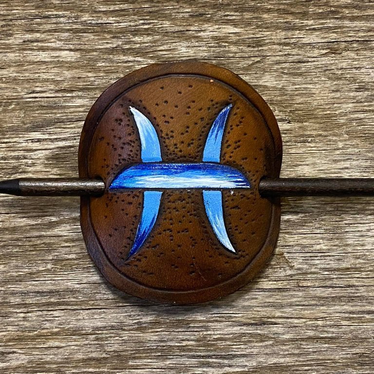 Sjalnæla eða hárnæla.   Stjörnumerki - Fiskarnir.  Handskorið í nautshúð og handlitað.  Þvermál sa. 10 cm.
Verð.  5.500,- iskr.