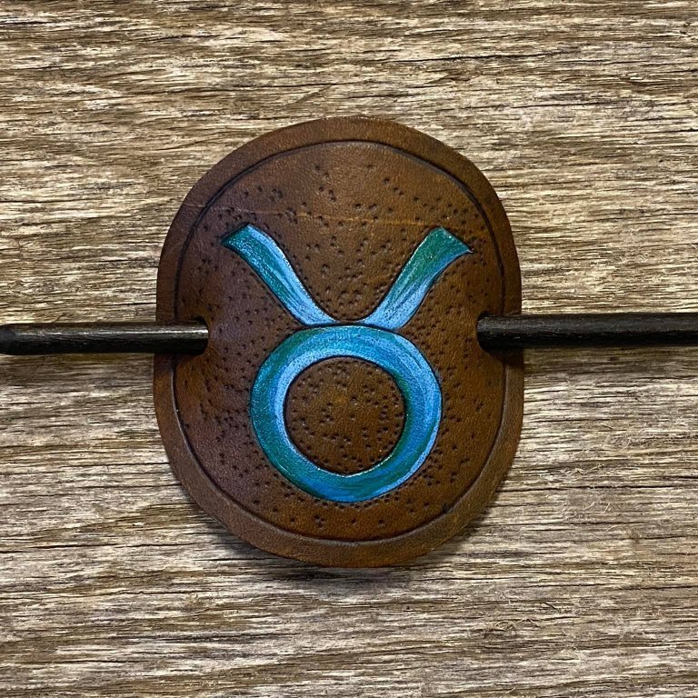 Sjalnæla eða hárnæla.   Stjörnumerki - Nautið.  Handskorið í nautshúð og handlitað.  Þvermál sa. 10 cm.
Verð.  5.500,- iskr.