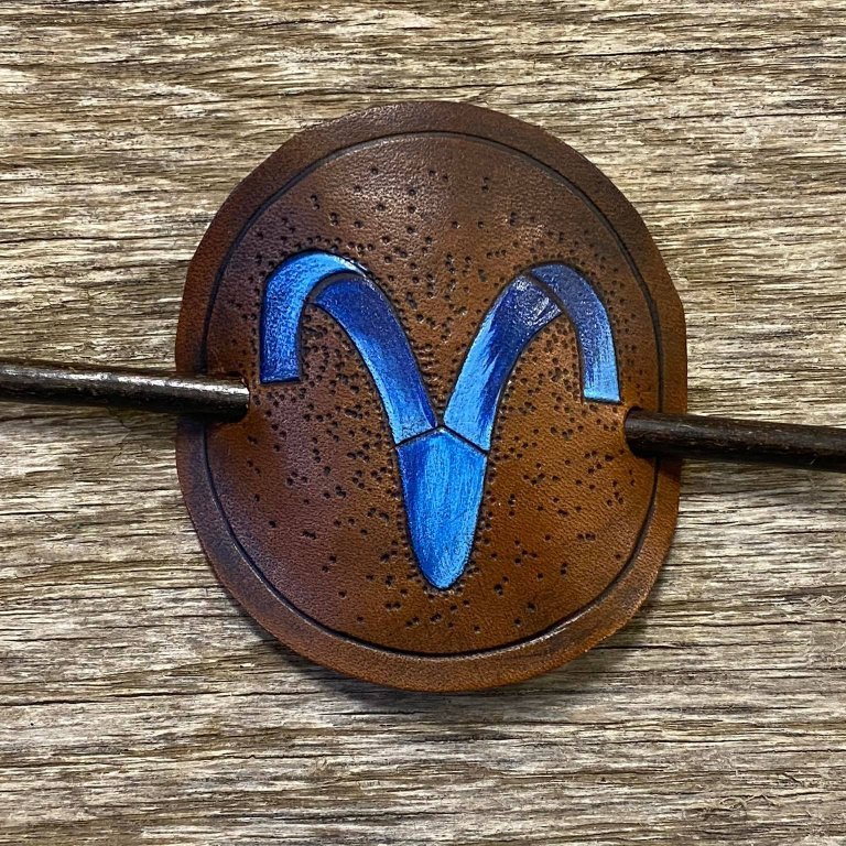 Sjalnæla eða hárnæla.   Stjörnumerki - Hrúturinn .  Handskorið í nautshúð og handlitað.  Þvermál sa. 10 cm.
Verð.  5.500,- iskr.