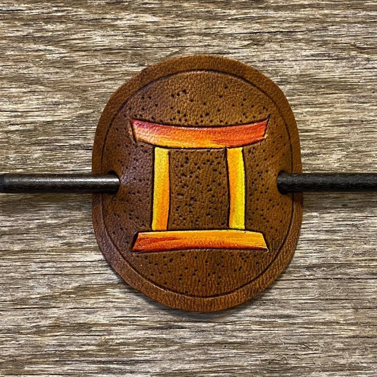 Sjalnæla eða hárnæla.   Stjörnumerki - Tvíburarnir.  Handskorið í nautshúð og handlitað.  Þvermál sa. 10 cm.
Verð.  5.500,- iskr.